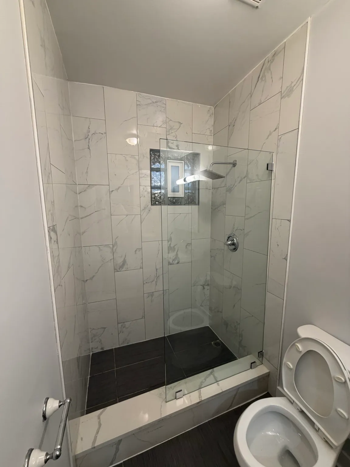 Finished bathroom shower with marble-look tile and frameless glass enclosure