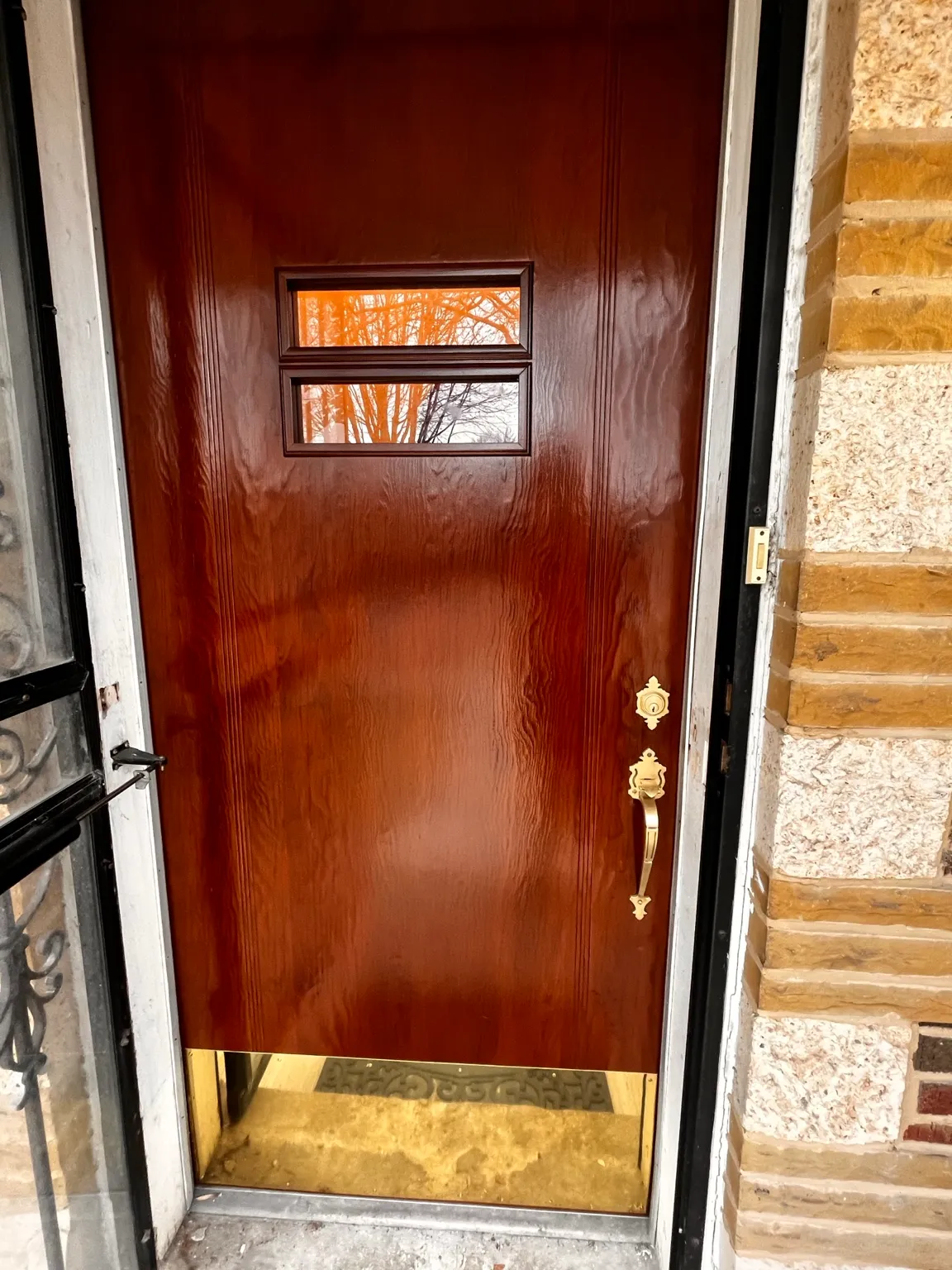 Finished rich red-brown wood entry door with polished brass hardware